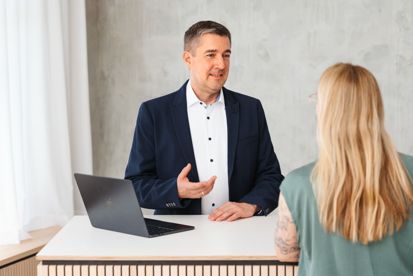 Andreas Luft im Gespräch mit einer Kundin, im Hintergrund ein MacBook